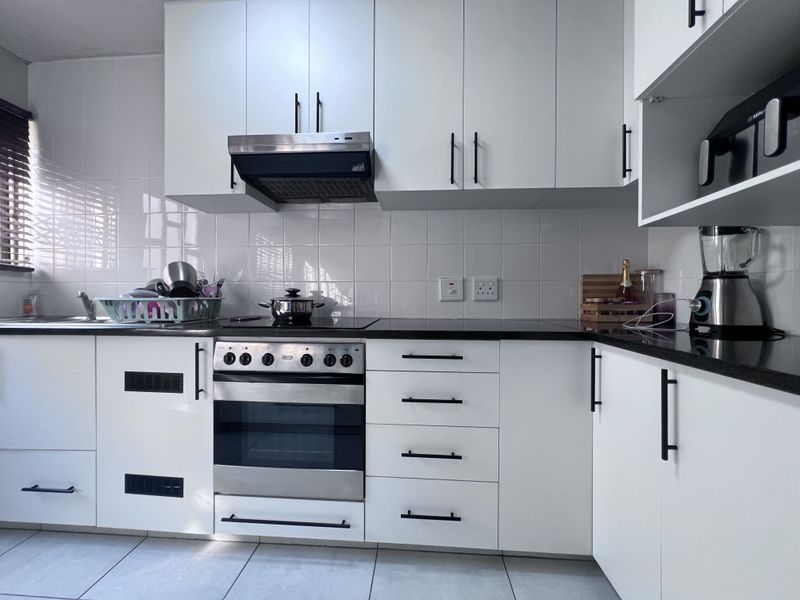 A modern, well-maintained kitchen featuring white cabinetry, black stone countertops, a built-in oven with hob, and a tiled splashback.