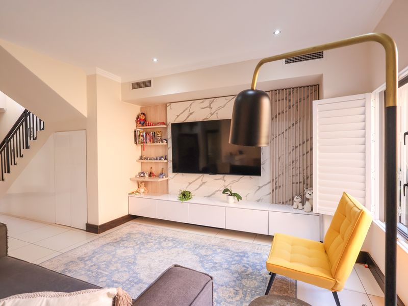 Modern living room featuring a marble-look media wall with built-in cabinetry, plantation shutters, and an adjacent staircase with a sleek metal balustrade.
