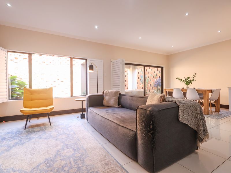 Bright open-plan living and dining area featuring large windows with plantation shutters, recessed downlighting, and polished tiled flooring throughout.