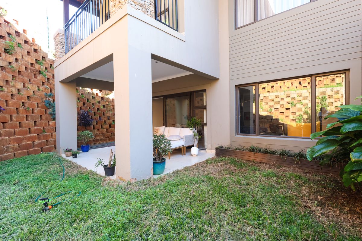 Rear view of the townhouse featuring a covered patio, a balcony above, and a tiered brick retaining wall bordering the garden area.