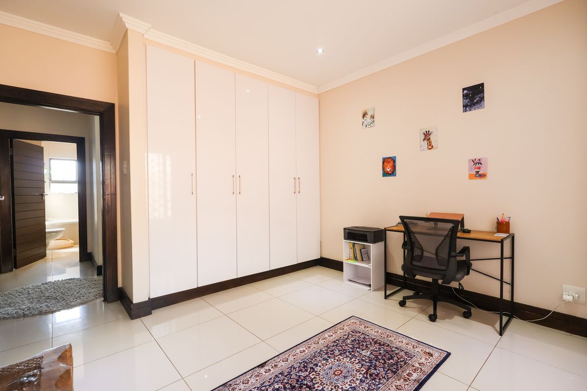 A well-maintained bedroom featuring glossy built-in cupboards, neutral tiled flooring, and recessed lighting, with an adjoining view into a bathroom.