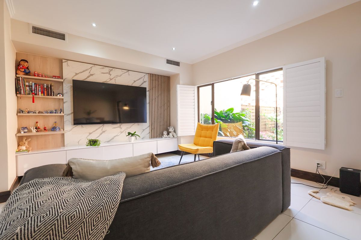 Modern living room featuring a marble-look media wall with built-in cabinetry, recessed lighting, ducted air conditioning, and plantation shutters overlooking the garden.