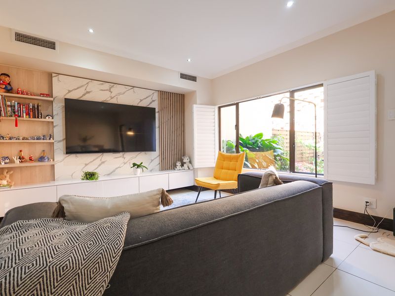 Modern living room featuring a marble-look media wall with built-in cabinetry, recessed lighting, ducted air conditioning, and plantation shutters overlooking the garden.