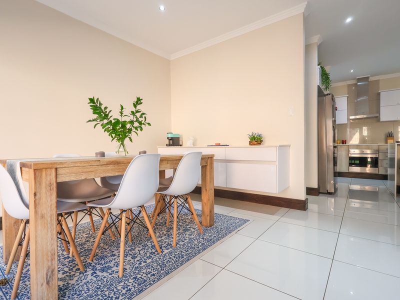 Open-plan dining area featuring polished porcelain tiles and recessed lighting, flowing into a modern kitchen equipped with built-in cabinetry and stainless steel appliances.