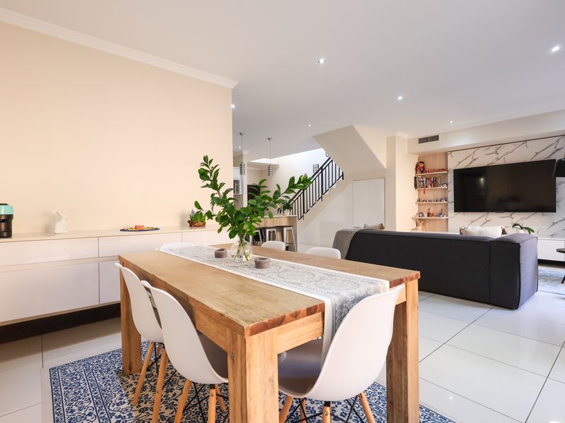 Spacious open-plan living and dining area featuring modern tiled floors, recessed lighting, and a striking marble-look feature wall with integrated media space.