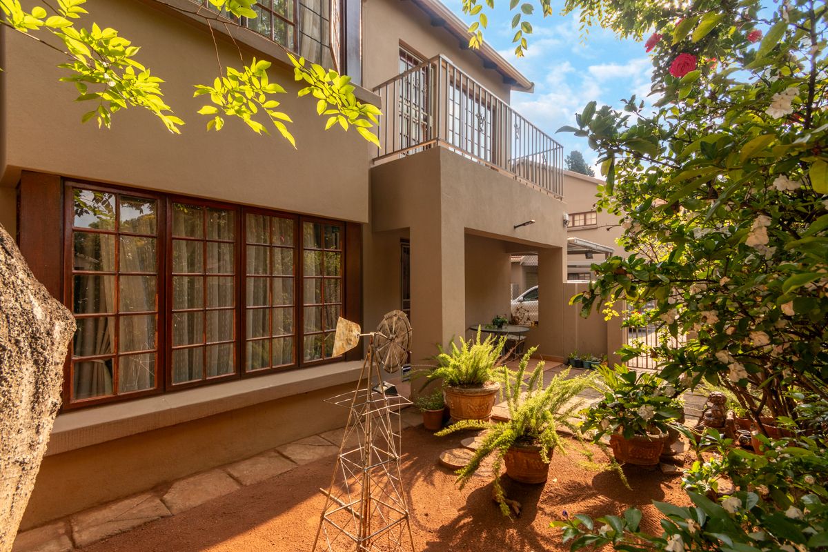 A well-maintained rear exterior view of the apartment featuring a private balcony with metal balustrade, timber-framed windows, and a paved patio area.