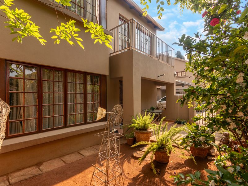 A well-maintained rear exterior view of the apartment featuring a private balcony with metal balustrade, timber-framed windows, and a paved patio area.