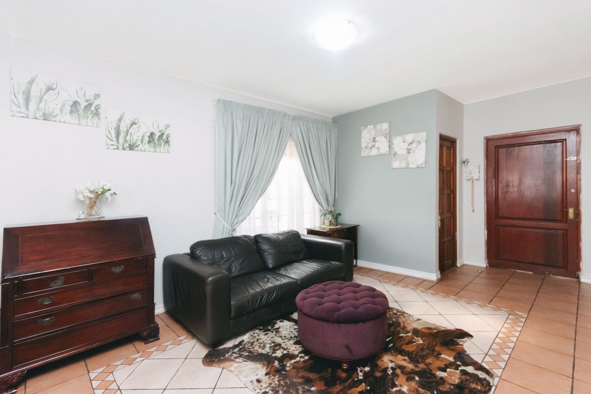 A living room featuring tiled flooring, a wooden entrance door, and a window with curtains.
