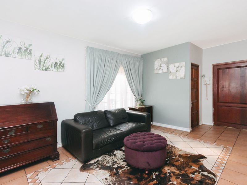 A living room featuring tiled flooring, a wooden entrance door, and a window with curtains.