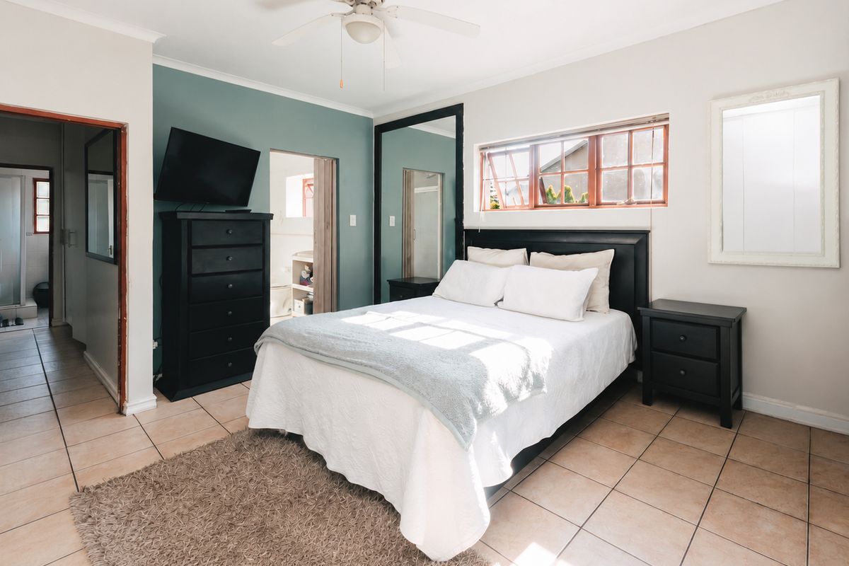 A bedroom featuring tiled flooring, a ceiling fan, and an en-suite bathroom. The room includes a built-in mirror wardrobe and natural light from the window.