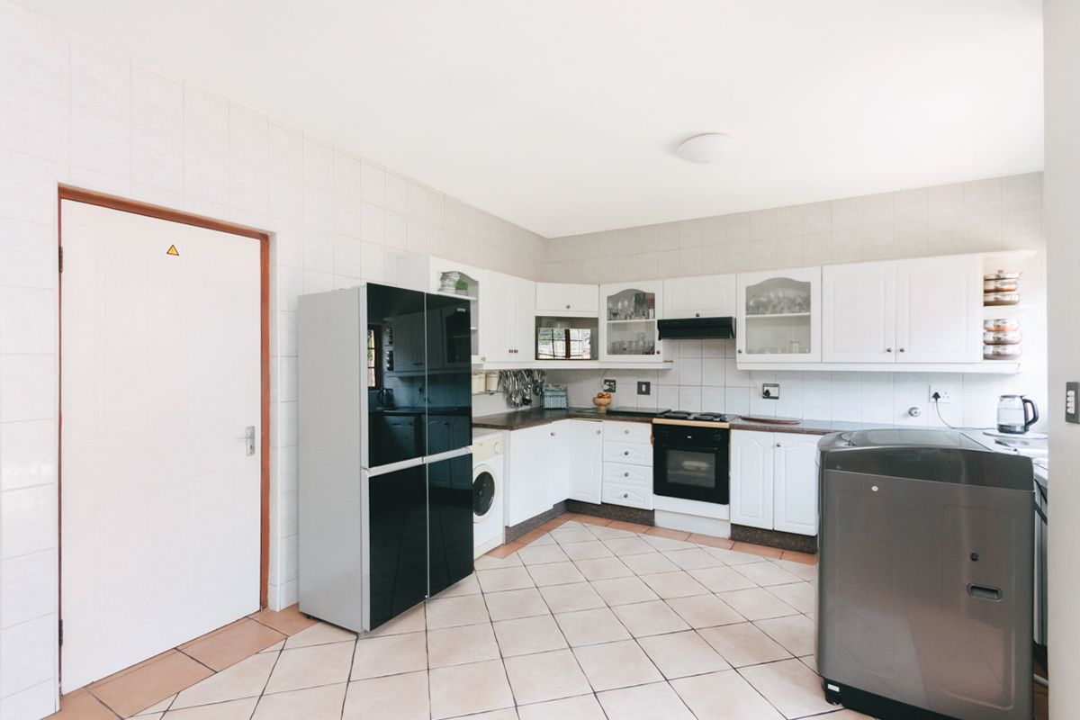 Functional kitchen featuring white cabinetry, tiled backsplash, built-in oven, extractor fan, and integrated laundry plumbing connections.