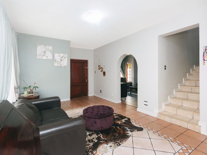 A living area featuring tiled flooring, an arched entryway leading to another room, and a staircase, providing a functional and connected layout.