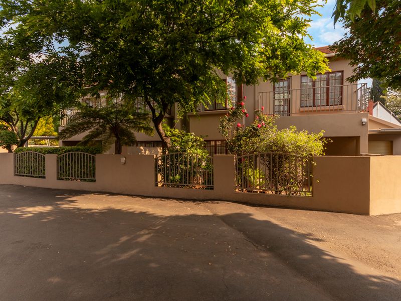 Front exterior view of the apartment complex featuring a paved driveway, perimeter wall with metal fencing, and upper-level balconies with railings.