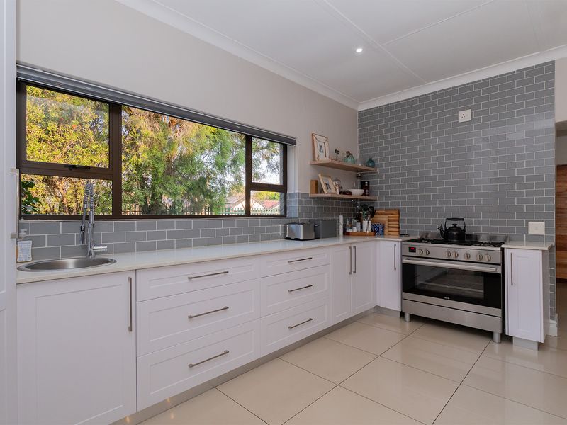 Modern kitchen featuring white shaker cabinetry, quartz countertops, grey subway tile backsplash, and a stainless steel gas stove with large window views.