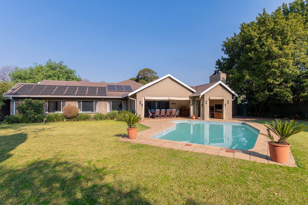 Rear view of the property featuring a spacious garden, swimming pool, covered patio with built-in braai, and roof-mounted solar panels.