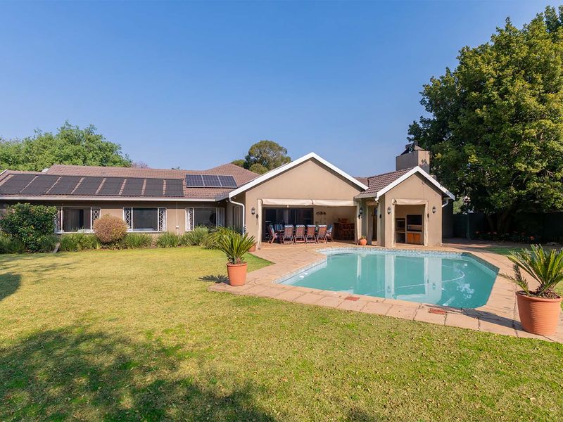Rear view of the property featuring a spacious garden, swimming pool, covered patio with built-in braai, and roof-mounted solar panels.