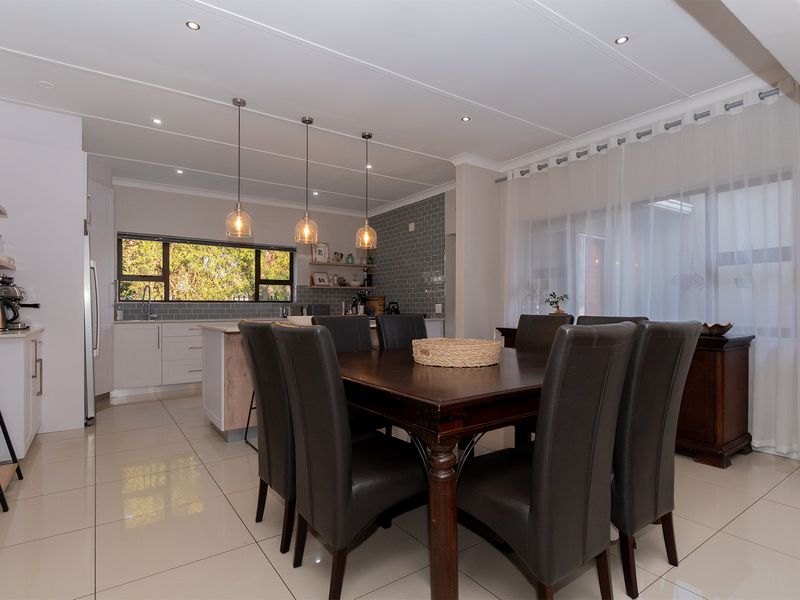 A bright open-plan kitchen and dining area featuring modern cabinetry, a central island, subway tile backsplash, and large sliding doors leading to the exterior.