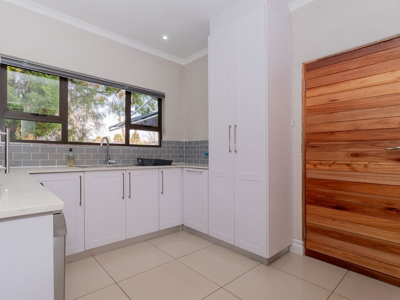 A clean and modern scullery featuring white built-in cabinetry, stone countertops, a stainless steel sink, and a stylish subway tile backsplash.