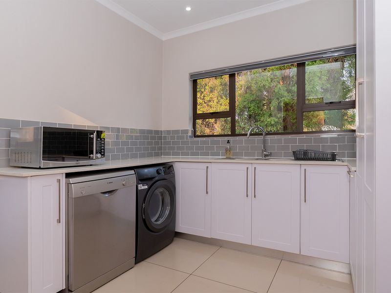 A clean and modern laundry room featuring white cabinetry, stone countertops, a subway tile backsplash, and tiled flooring with a large window.