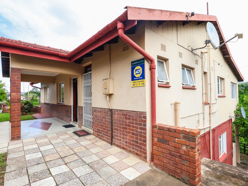 Side view of the house featuring a covered tiled patio, brick facade, and security gate entrance.