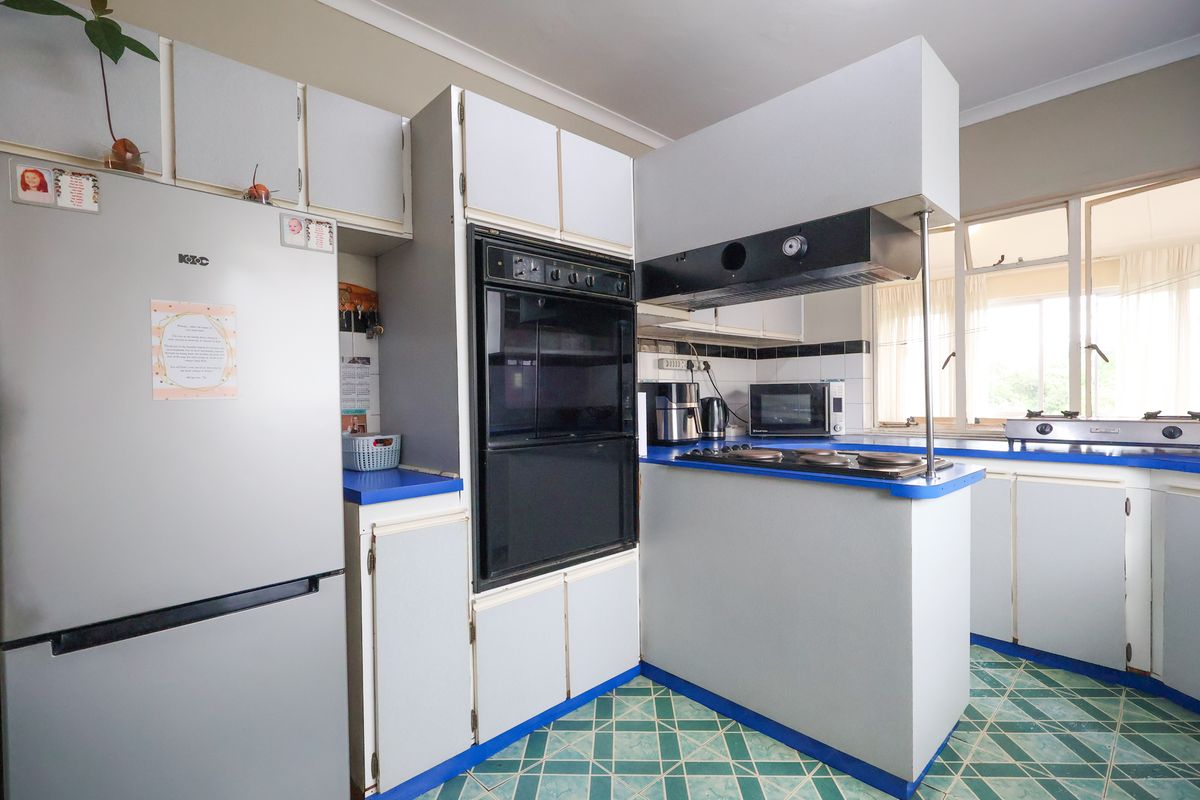 A functional kitchen featuring built-in oven, electric hob, extractor fan, and tiled flooring, offering a dated layout ready for modern renovation.