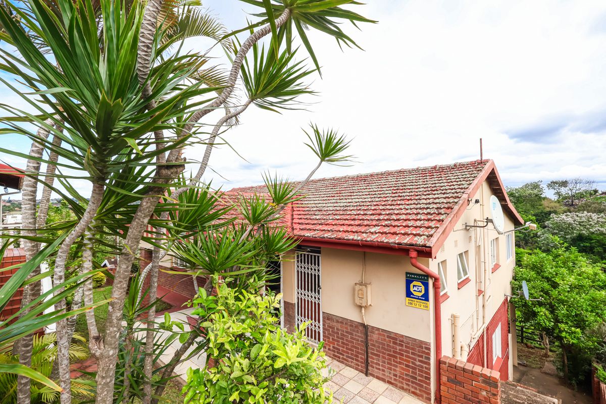 Rear exterior view of the property featuring a tiled roof, brick and plaster facade, and a paved walkway leading to a security gate.