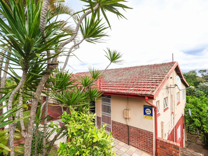 Rear exterior view of the property featuring a tiled roof, brick and plaster facade, and a paved walkway leading to a security gate.