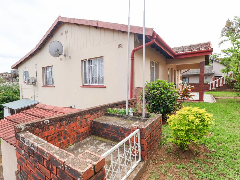 Rear view of the house featuring a brick retaining wall, tiled roof, and a covered patio area set within a garden.