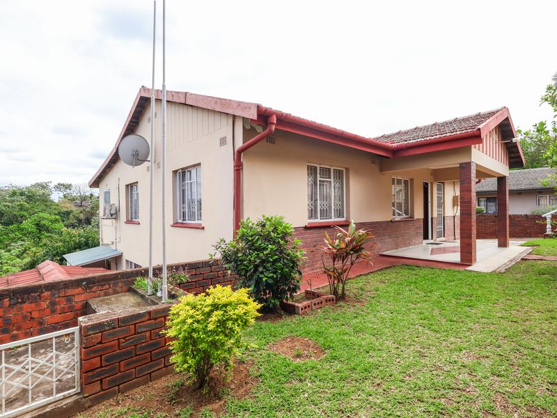 Rear view of the house featuring a covered patio, brick retaining wall, and established garden area with tiled roof structure.