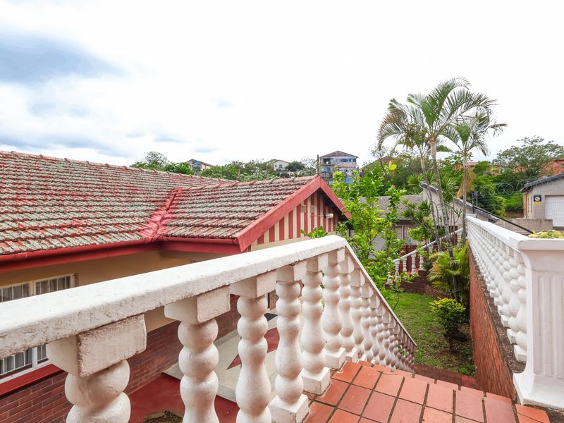 Rear exterior view featuring a tiled roof, brick staircase with a decorative balustrade, and a retaining wall leading to a garden area.