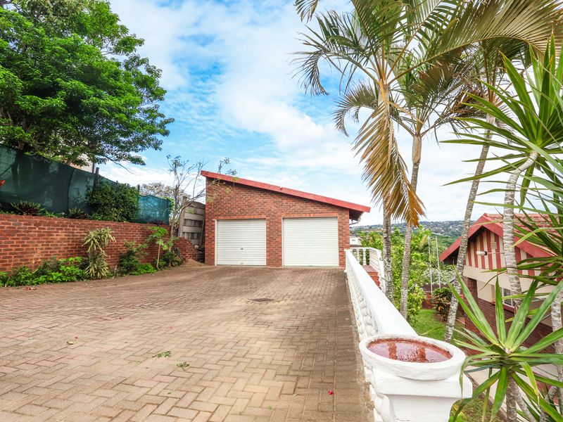 A detached double garage with a brick exterior, featuring a spacious paved driveway and surrounding landscaped garden area.