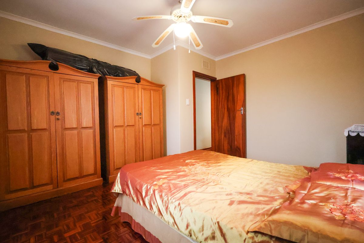 A bedroom featuring parquet flooring, a ceiling fan, and a timber door, providing a functional and traditional living space.