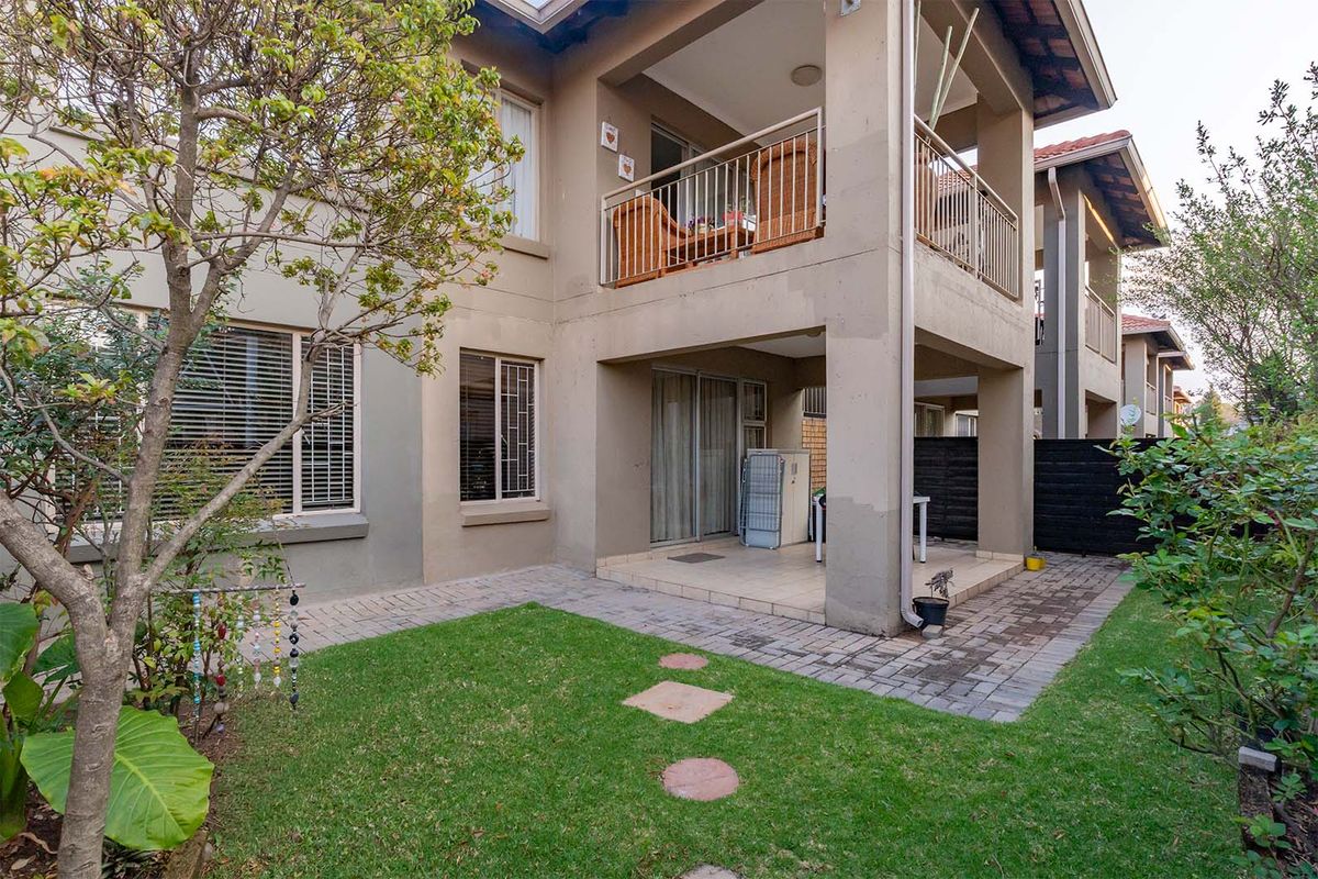 Rear view of the apartment featuring a ground floor covered patio, an upper-level balcony with metal railings, and a small private garden area.