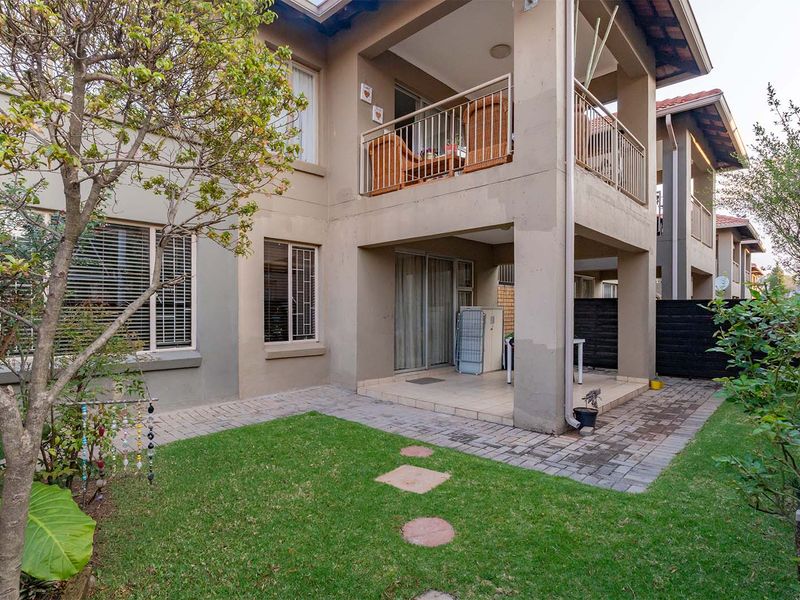 Rear view of the apartment featuring a ground floor covered patio, an upper-level balcony with metal railings, and a small private garden area.