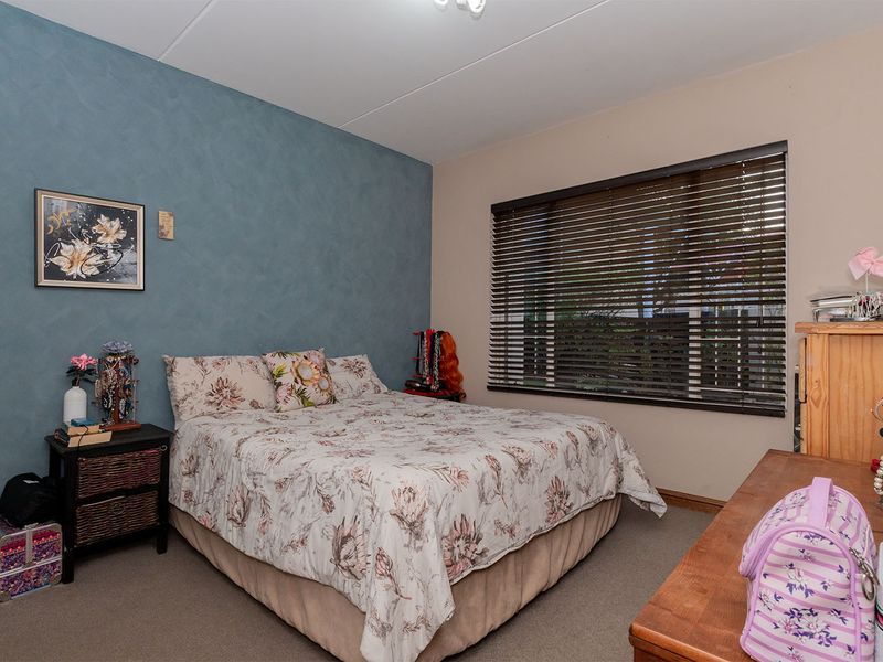 A bedroom featuring carpeted flooring, a blue accent wall, and fitted venetian blinds over the window.
