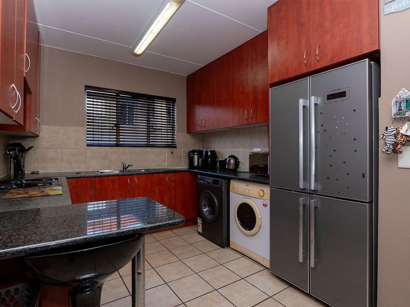 Functional kitchen featuring dark wood cabinetry, granite countertops, tiled backsplash, and integrated space for laundry appliances.