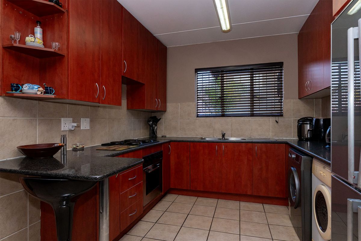 A functional kitchen featuring cherry-wood cabinetry, granite countertops, a built-in oven with gas hob, and tiled finishes throughout.