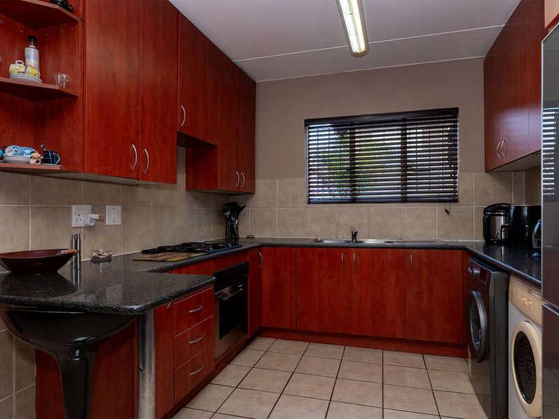 A functional kitchen featuring cherry-wood cabinetry, granite countertops, a built-in oven with gas hob, and tiled finishes throughout.