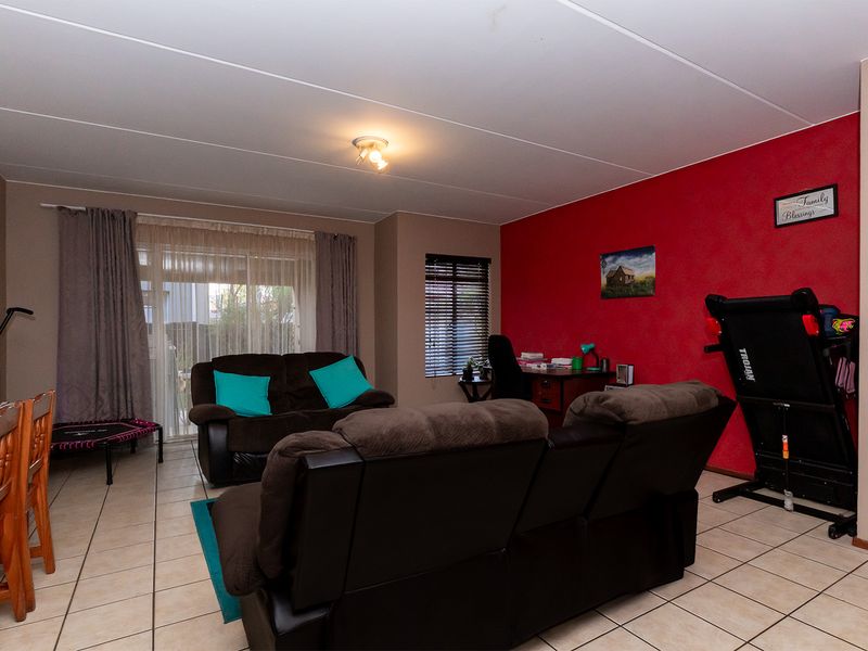 Spacious living area featuring tiled flooring, a sliding glass door providing natural light, and a prominent red accent wall.