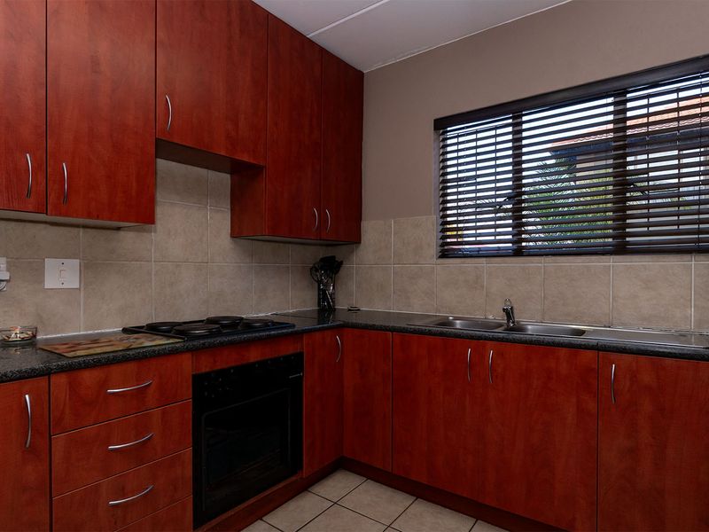 Functional kitchen featuring cherry-toned cabinetry, granite countertops, built-in oven, electric hob, and a double bowl sink with tiled backsplash.