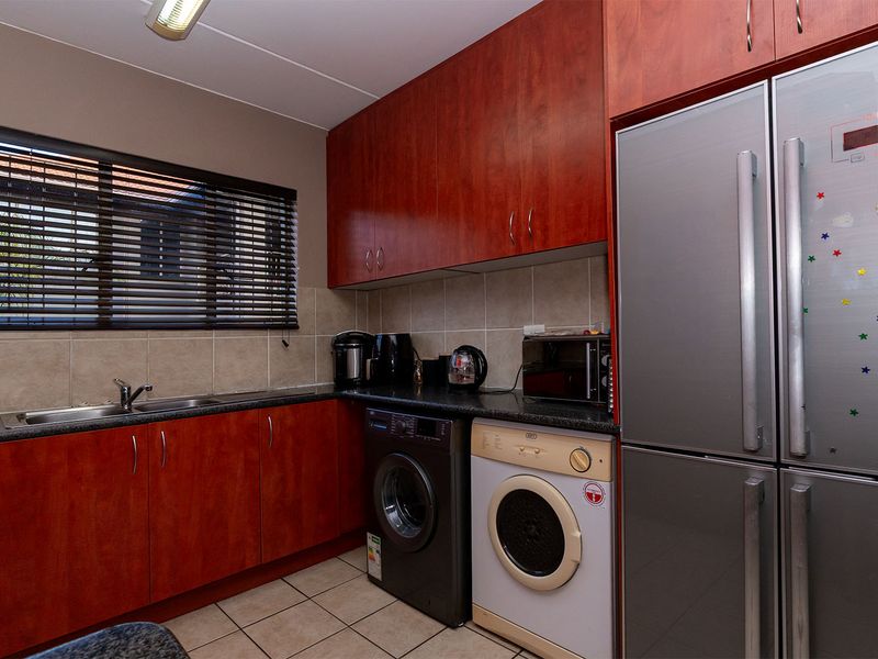 Functional kitchen featuring wood-finish cabinetry, dark laminate countertops, tiled backsplash, and dedicated spaces for laundry appliances and a large refrigerator.
