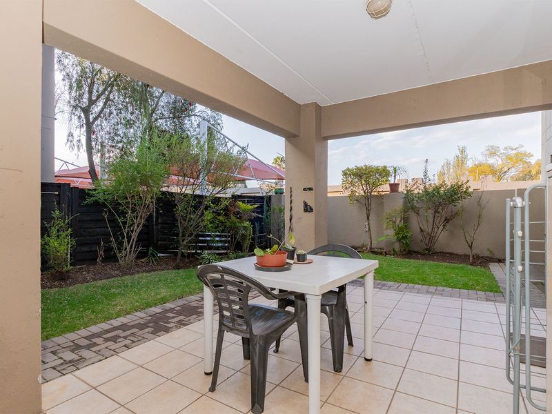 A covered patio area featuring tiled flooring and concrete pillars, overlooking a private garden space with boundary walls.