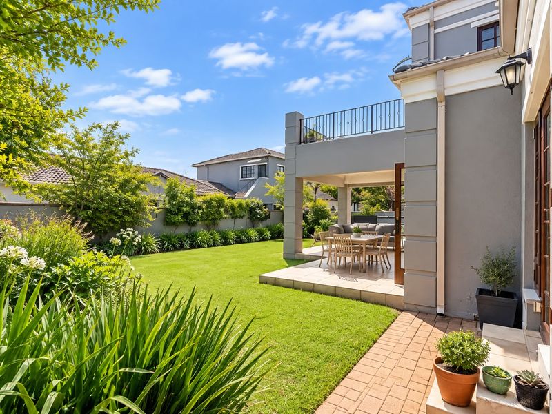 A well-maintained rear garden featuring a manicured lawn, a covered patio area, and an upper-level balcony with metal railings.