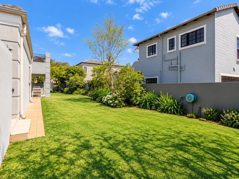 A well-maintained rear garden featuring a lush green lawn, paved walkway, and perimeter boundary wall, providing a private outdoor space.