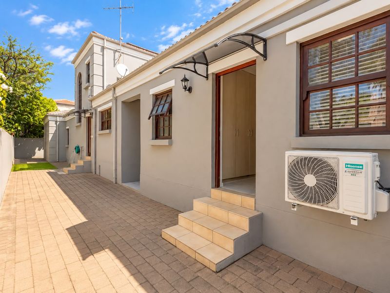 A well-maintained rear exterior view featuring a paved courtyard, tiled access steps, and an external air conditioning unit mounted to the building facade.