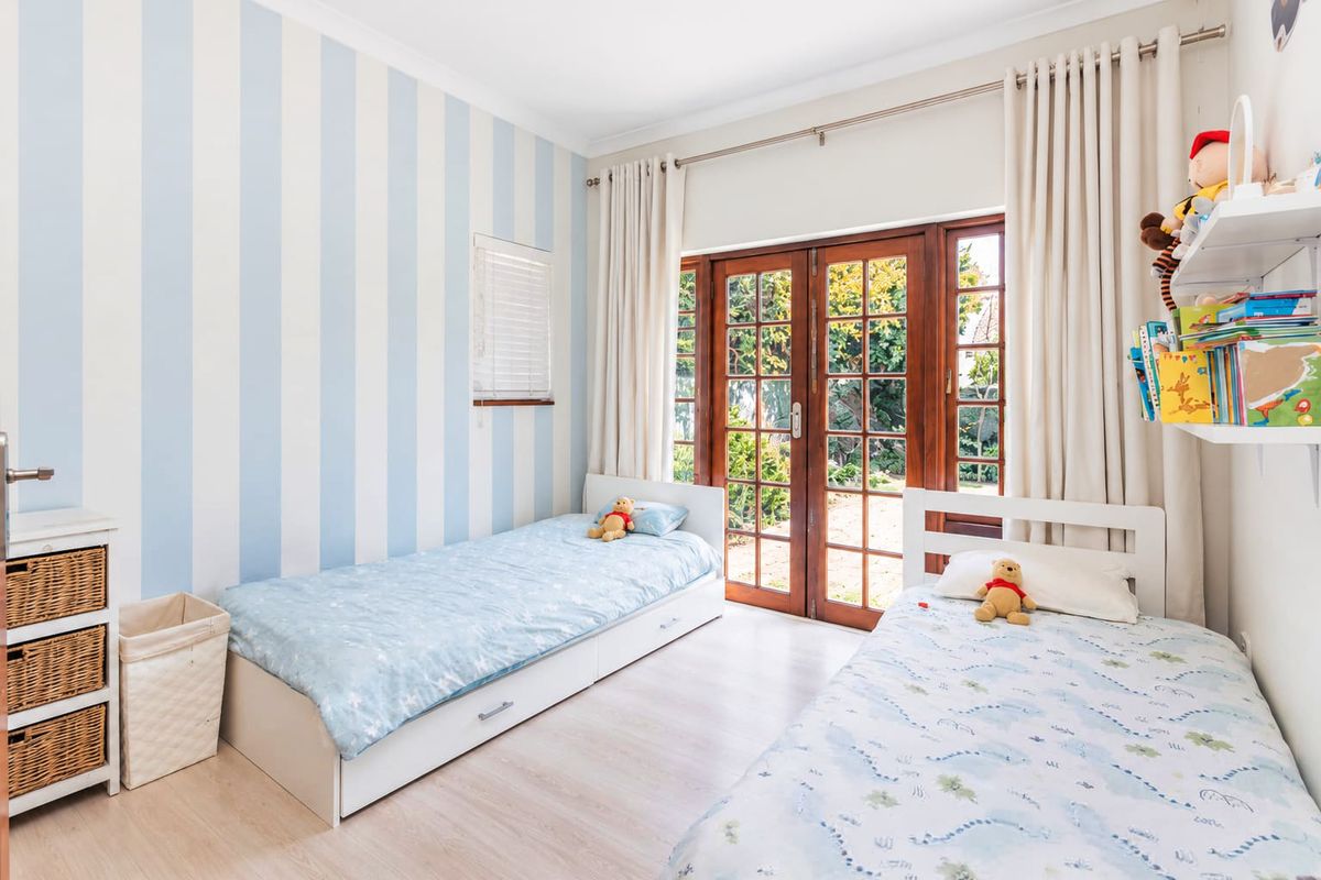 A bright bedroom featuring light-toned laminate flooring, striped wallpaper, and wooden French doors providing direct access to the garden.