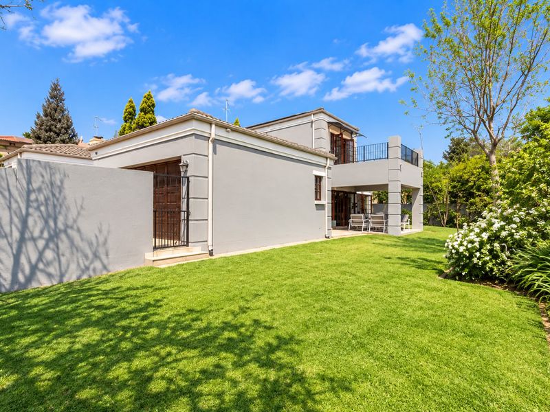 Rear view of the property featuring a well-maintained lawn, a covered patio area, and an upper-level balcony with wrought iron railings.
