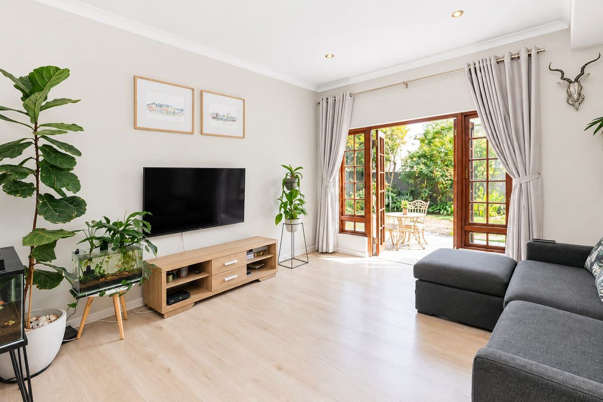 Bright living room featuring light timber-look flooring, recessed downlights, and timber-framed french doors providing direct access to the rear garden.
