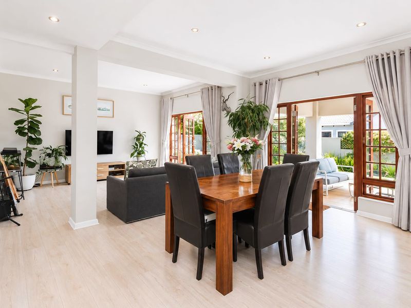Spacious open-plan living and dining area featuring light laminate flooring, recessed lighting, and double wooden doors leading to an outdoor patio.