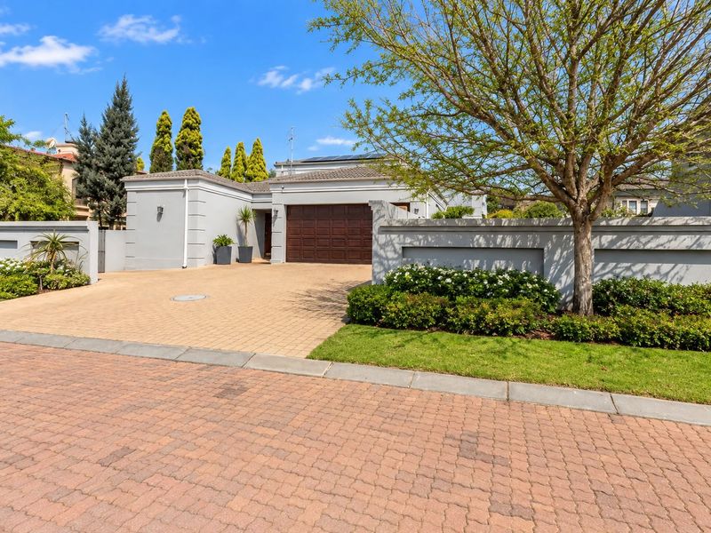 A well-maintained front exterior featuring a paved driveway, double garage, and secure boundary wall with established garden landscaping.